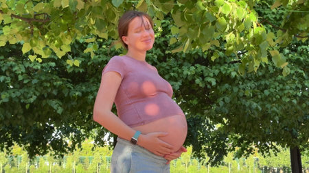 beautiful pregnant young woman walking in park in warm summer weather enjoying third trimester