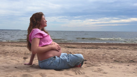 Happy pregnant young woman with big belly sitting on the beach near seaの写真素材