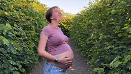beautiful pregnant young woman walking in park in warm summer weather enjoying third trimester in...