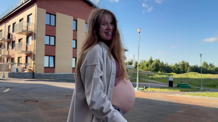 Beautiful happy pregnant young woman is smiling and stroke her belly at homeの写真素材