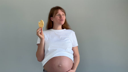 Happy pregnant young woman eating snack food with big bellyの写真素材