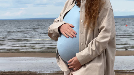 Unrecognizable young pregnant woman walking outdoors on the beach and stroking her bellyの写真素材