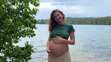 Happy pregnant young woman walking in the park with a big belly