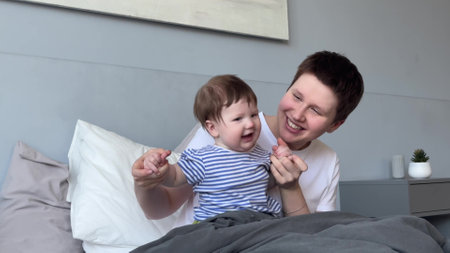 young mom of toddler having fun with baby in bed during daytime