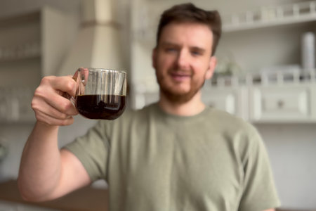 Happy young man is drinking coffee in the morning at a kitchen and smileの写真素材