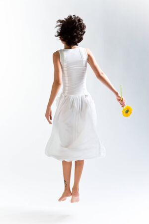 Young woman in with dress jumping up with flowerの写真素材