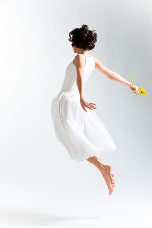 Young woman in with dress flying with flower