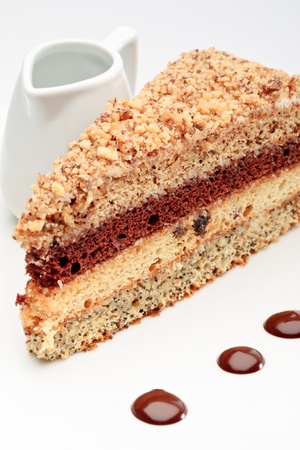A piece of fresh baked delicious sponge-cake with chocolate sauce on a white plate. A hand pouring chocolate sauce out of a sauceboat on it.の写真素材