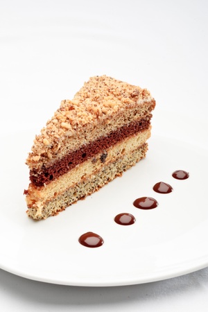 A piece of fresh baked delicious sponge-cake with chocolate sauce on a white plate. A hand pouring chocolate sauce out of a sauceboat on it.の写真素材