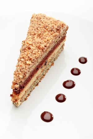 A piece of fresh baked delicious sponge-cake with chocolate sauce on a white plate. A hand pouring chocolate sauce out of a sauceboat on it.の写真素材