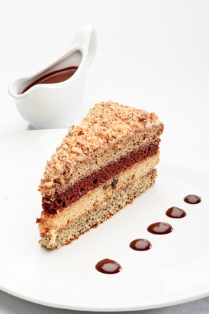 A piece of fresh baked delicious sponge-cake with chocolate sauce on a white plate. A hand pouring chocolate sauce out of a sauceboat on it.の写真素材