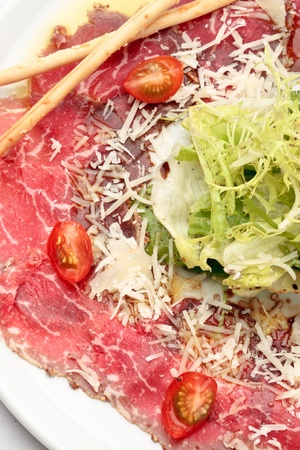 Beef carpaccio with lettuce, tomatoes and parmesan on a white plateの写真素材