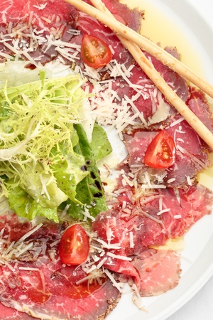 Beef carpaccio with lettuce, tomatoes and parmesan on a white plateの写真素材