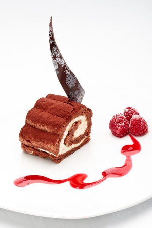 Chocolate roll with crud and mango cream decorated with raspberry and sauce on a white backgroundの写真素材