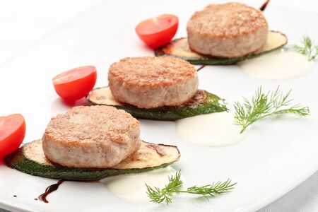 Russian chicken cutlets decorated with tomatoes and squash on a white backgroundの写真素材