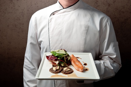 a chief dressed in white holding a white tray with roasted salmon fillet and vegetable salad elegantly decoratedの写真素材