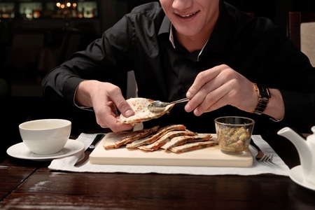 A handsome young man eating delicious arabian pita with rice and vegetable stuffing at a table elegantly servedの写真素材