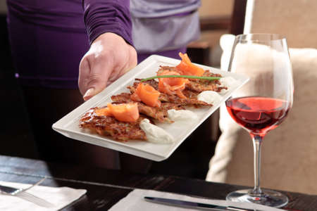 A mans hand holding a white tray with crispy potato pancakes decorated with salmon and sour creamの写真素材