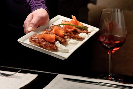 A mans hand holding a white tray with crispy potato pancakes decorated with salmon and sour creamの写真素材