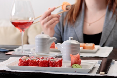 Two sets of California maki sushi roll on white plates elegantly decorated, a woman eating maki with chopsticks on a backgroundの写真素材