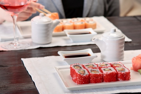 Two sets of California maki sushi roll on white plates elegantly decorated, a woman eating maki with chopsticks on a backgroundの写真素材