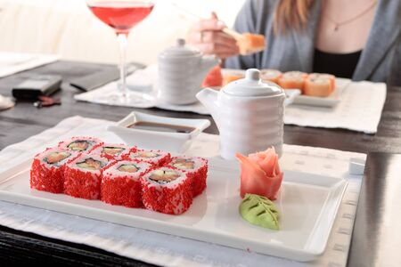 Two sets of California maki sushi roll on white plates elegantly decorated, a woman eating maki with chopsticks on a background Two sets of California maki sushi roll on white plates elegantly decorated, a woman eating maki with chopsticks on a background