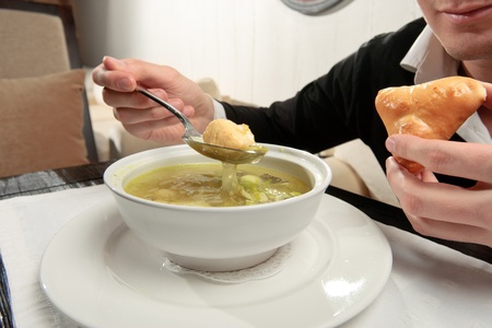 A young man eating fish soup, sitting at a table elegantly served in a restaurant, close upの写真素材