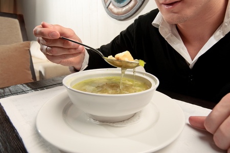 A young man eating fish soup, sitting at a table elegantly served in a restaurant, close upの写真素材