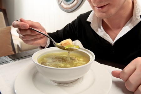 A young man eating fish soup, sitting at a table elegantly served in a restaurant, close upの写真素材