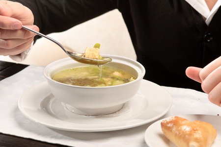 A young man eating fish soup, sitting at a table elegantly served in a restaurant, close upの写真素材