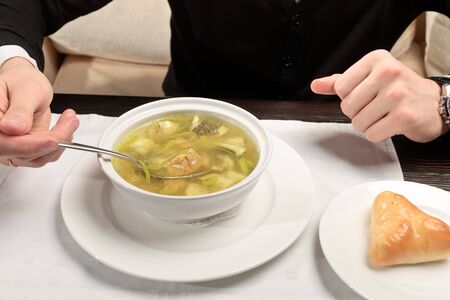 A young man eating fish soup, sitting at a table elegantly served in a restaurant, close upの写真素材