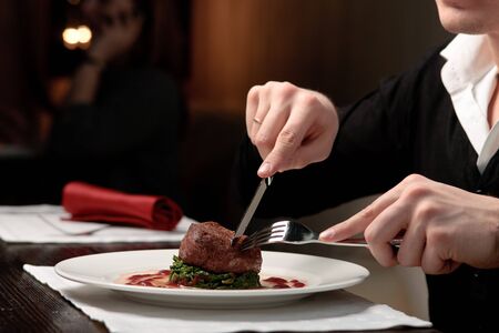 A handsome young man eating delicious meat cutlet with a knife and fork at a table elegantly servedの写真素材