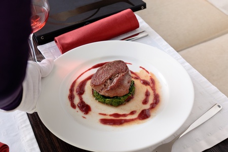 Meat cutlet placed on a spinach cutlet on a white plate decorated with tomato sauce, on a table elegantly servedの写真素材