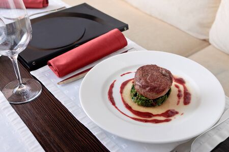 Meat cutlet placed on a spinach cutlet on a white plate decorated with tomato sauce, on a table elegantly servedの写真素材