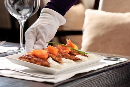 Crispy potato pancakes decorated with salmon and sour cream being served by a waiterの写真素材