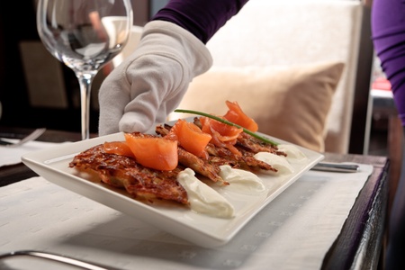 Crispy potato pancakes decorated with salmon and sour cream being served by a waiterの写真素材