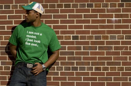Attractive young African American male playing posing in a green t-shirt and jeans against a brick...