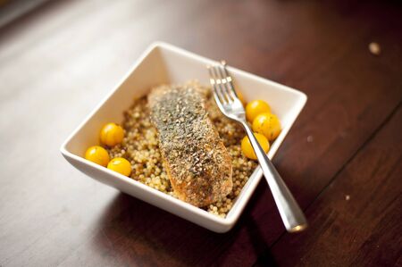 An Alaskan wild salmon grilled and seasoned on a cedar plank placed on top of a couscous with tomatoes on a wooden table.の写真素材