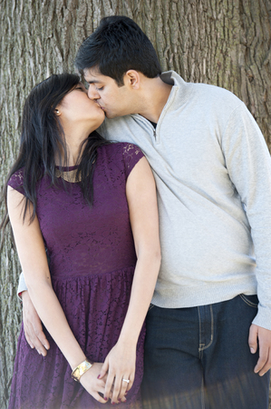 A young and happy Indian couple kissing with a tree background on a cloudy day.の写真素材