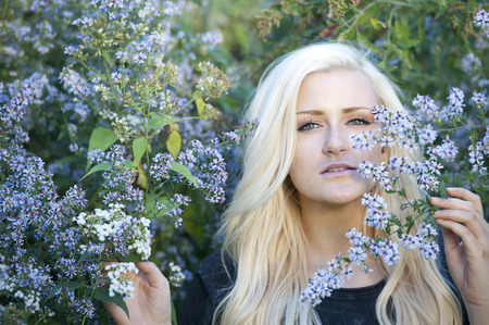 A young attractive female blond posing near blue flowers on a sunny day.の写真素材