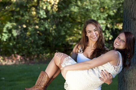 A young brunette girl carrying her friend outdoors at a park on a sunny day.の写真素材