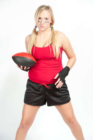 A female blond model holding a red and black football wearing a red t-shirt with black shorts on a white background.の写真素材
