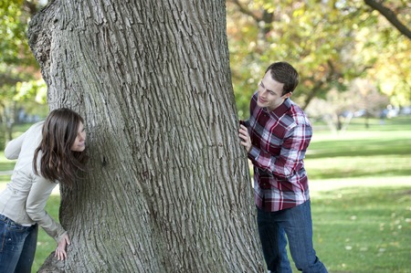 Happy young couple looking for each other around a tree.の写真素材