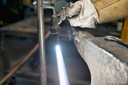 A metal fabricator utilizing a torch to heat up a piece of metal in order to shape it.