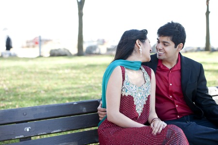 A young and happy Indian couple posing on a park bench in the Fall.