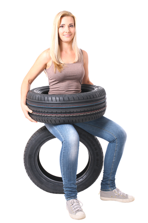 A beautiful young blond girl sitting on a black tyre. Isolated on white.の写真素材