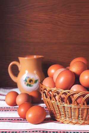 Fresh chicken eggs in a woven basket on a ornamented towel and wooden background. Easter, nutrition and diet stock imageの写真素材