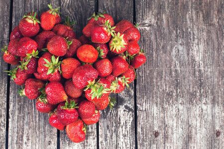 Fresh farmer strawberries on dark wood texture in shape of heartの写真素材