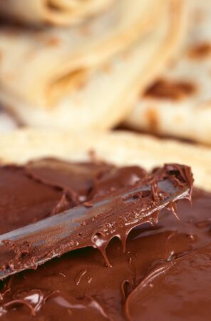 Breakfast photograph of knife spreading chocolate paste on a pancake. Macro shallow depth of field