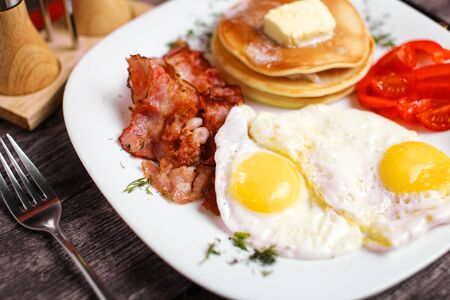 Tasty breakfast with fried eggs, pancakes, bacon and vegetables. の写真素材